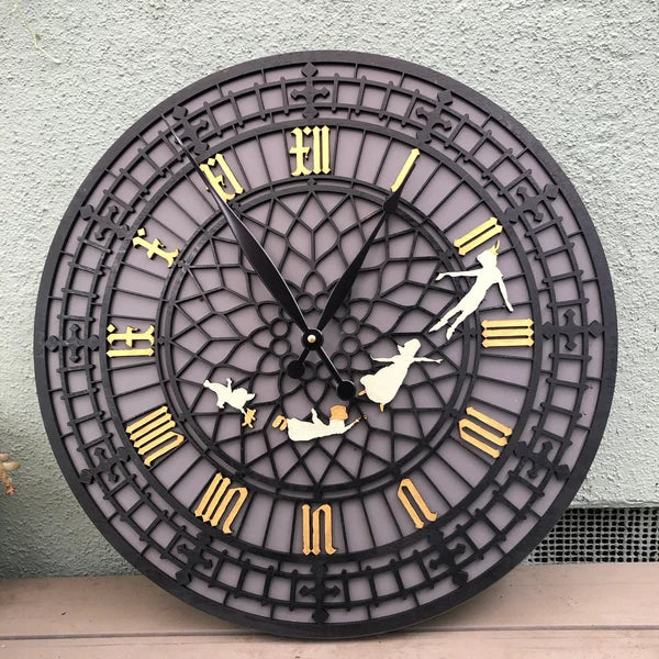 Decorative wall clock with black frame, gold Roman numerals, and white figures on a light gray wall.
